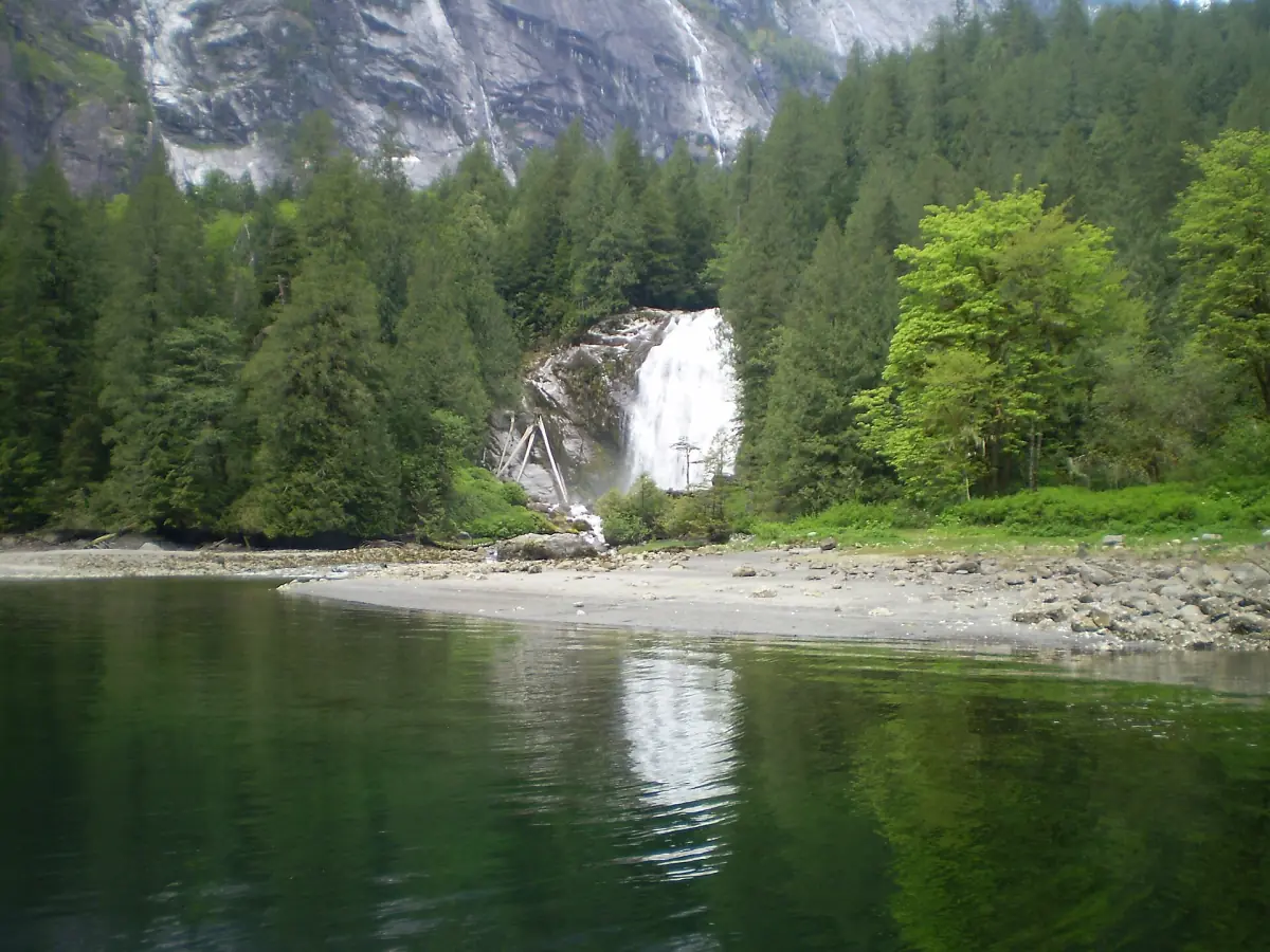 Die Chatterbox Falls stürzen durch Wald auf ein felsiges Ufer neben grünem Wasser