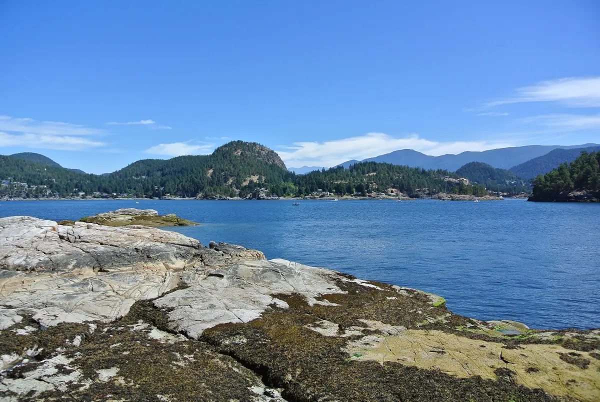 Blaues Wasser und bewaldete Hügel, gesehen von einem felsigen Ufer bei Pender Harbour