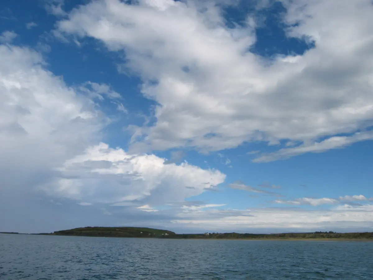 Porpoise Bay unter blauem Himmel mit weißen Wolken und einer niedrigen bewaldeten Insel