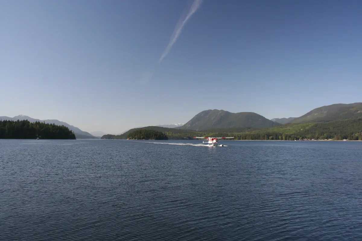 Kleines Flugzeug über dem ruhigen Wasser der Porpoise Bay mit dunstigen Bergen dahinter