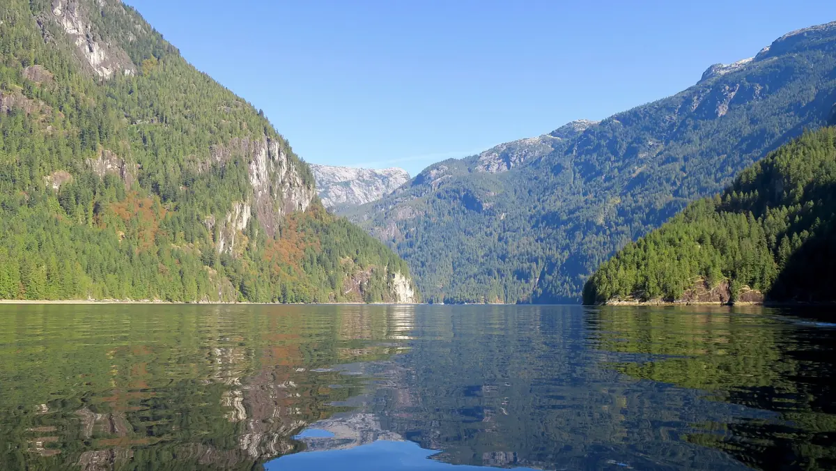 Granitfelsen und bewaldete Hänge spiegeln sich im stillen Wasser des Princess Louisa Inlet