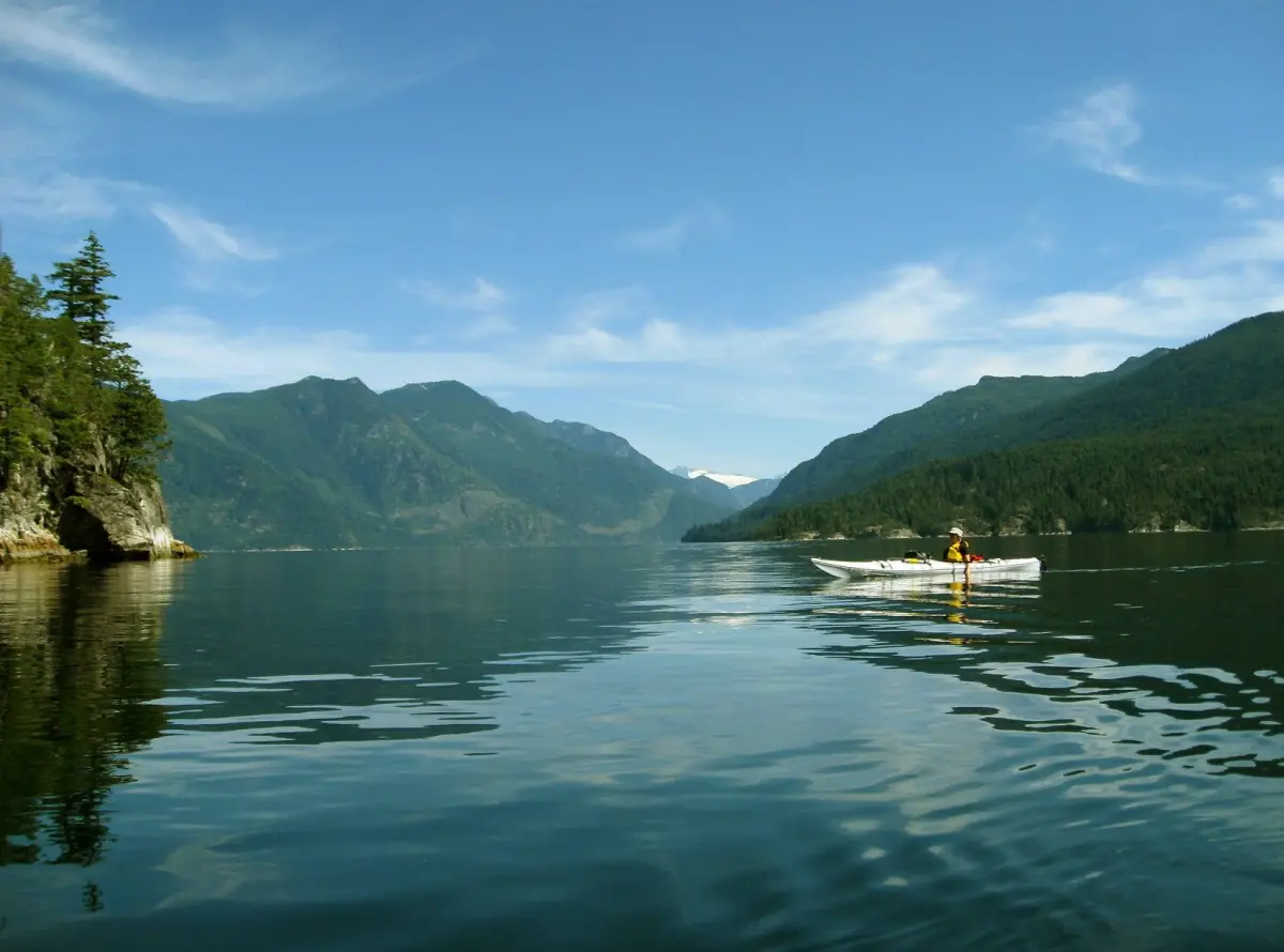 Kajakfahrer paddelt über das grüne Wasser des Sechelt Inlet zwischen bewaldeten Bergufern