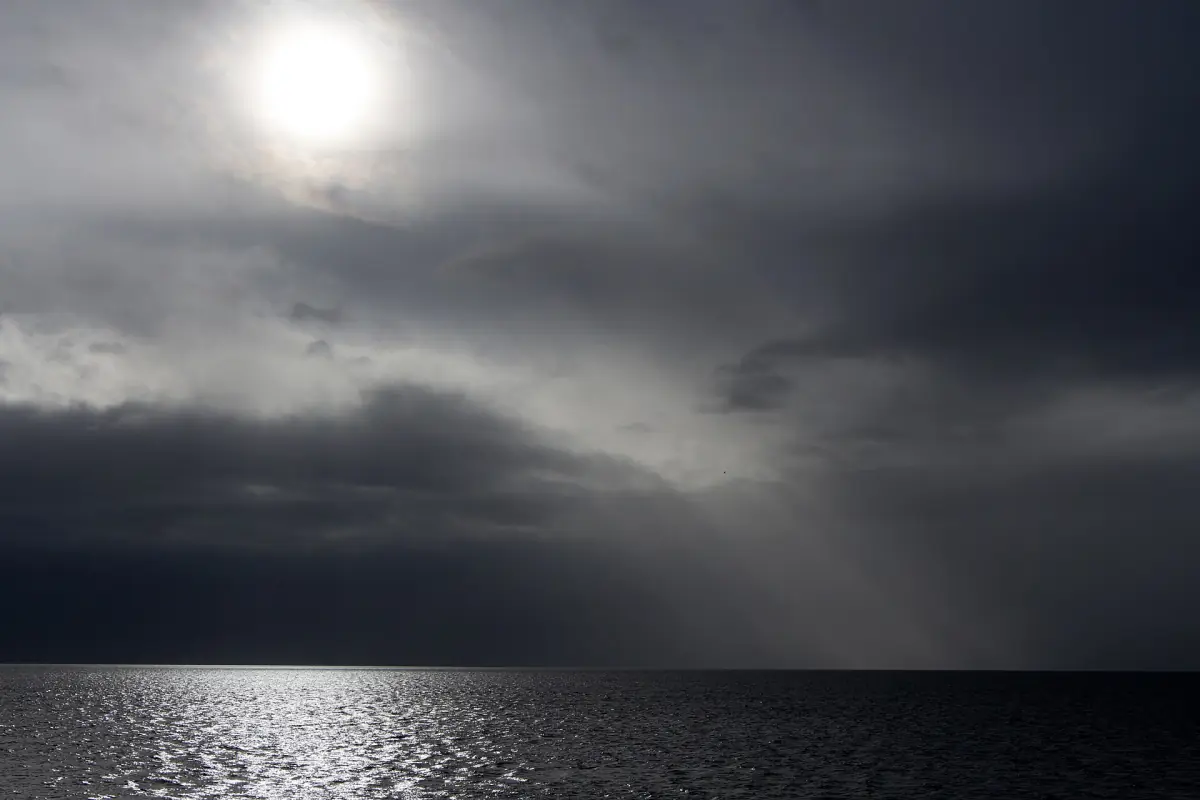 Dunkle Gewitterwolken über dem Meer, durch die die Sonne bricht